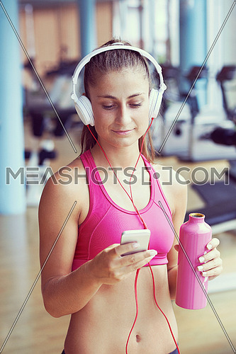 young healthy woman drinking water  in fitness gym while sitting on pilates ball and listening music on headphones from smartphone