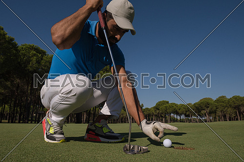 close up of man's hand putting golf ball in hole at course