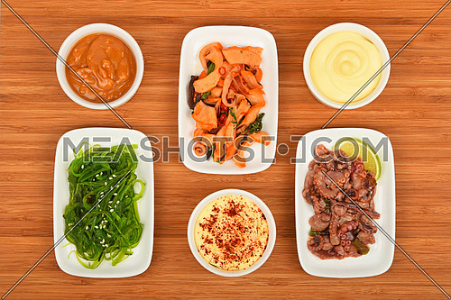Three portions of seafood marinated salad with octopus cuttlefish, squid and seaweeds in white plates with sauce on wooden table, high angle view