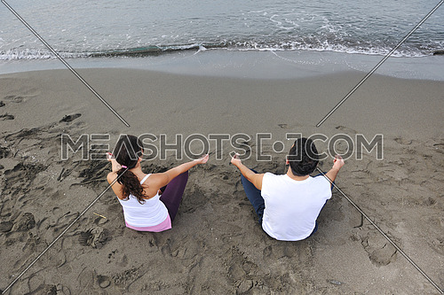 young couple people meditating yoga in lotus position at early morning on the beach