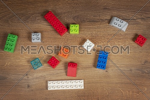 Top view on colorful toy bricks on a brown wooden background. Toys in the table