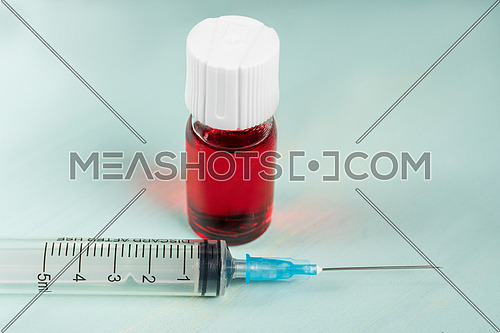 medical vaccine vials with red liquid and syringe over green table and white background. Vaccination and immunization conceptual.