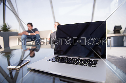 modern laptop with empty screen at modern office interior, business people group in background working together