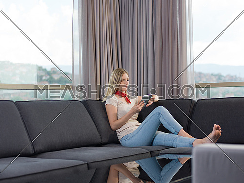 beautiful young woman on sofa at home surfing  internet using tablet computer
