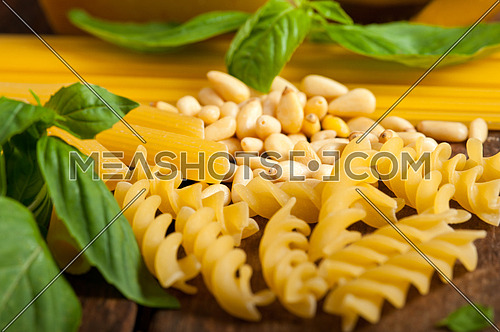 Italian basil pesto ingredients and raw pasta over old wood macro