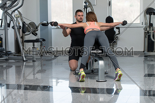 Personal Trainer Showing Young Woman How To Train Back Exercise With Dumbbells In A Health And Fitness Concept