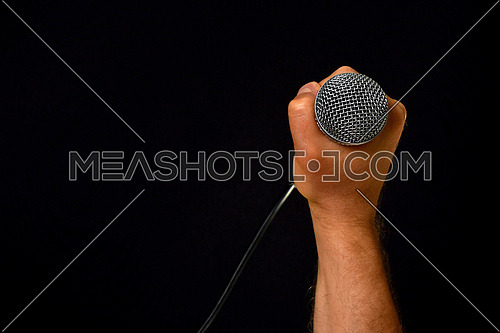 Male hand holding microphone with wire cable isolated on black background