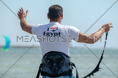 Male Kite surfing instructor wearing a white shirt wiritten on ( I Love Egypt) and  Egyptian flag heart shaped giving instruction to surfers  in the Red Sea by day.