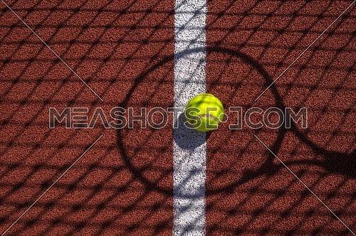 Shadows of net and racket surrounding a tennis ball on a white line on an outdoor court in sunshine in a sport and active lifestyle concept