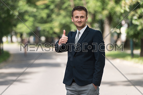 Portrait Of Confident Businessman While Standing Outdoors In Park Showing Thumbs Up Sign