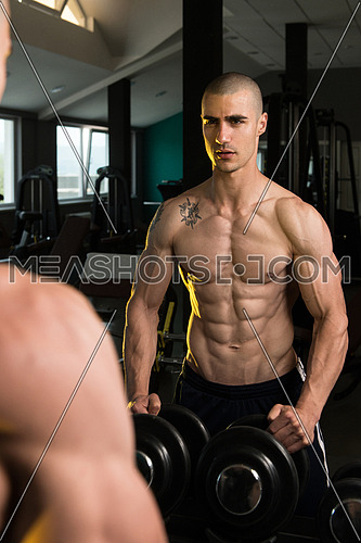 Young Man Standing Strong In Front Of A Mirror And Flexing Muscles - Muscular Athletic Bodybuilder Fitness Model Posing After Exercises