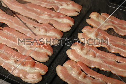 Close up cooking several bacon slices, rashers, on electric grill surface, high angle view