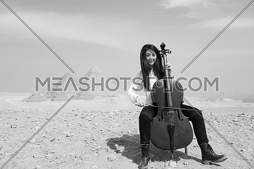black and white shot of young female cello player in egyptian desert with pyramids in background