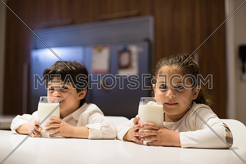 little middle east boy and girl eating snacks and drinking milk in the kitchen with pleasure