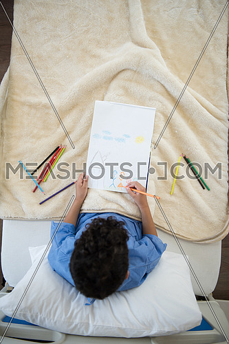 top view of little middle eastern boyl painting home and family at hospital bed