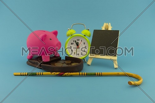 Saving for old-age and retirement concept with open purse with coins, walking stick, alarm clock and piggy bank over a blue background with copy space