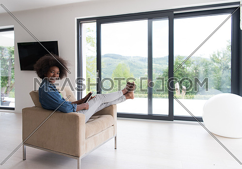 Young african american woman at home relaxing in her luxury lliving room reading a digital tablet PC surf internet and work
