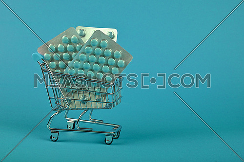 Close up several different blister packs of pills in small shopping cart over blue background, concept of online medicine order delivery, low angle view