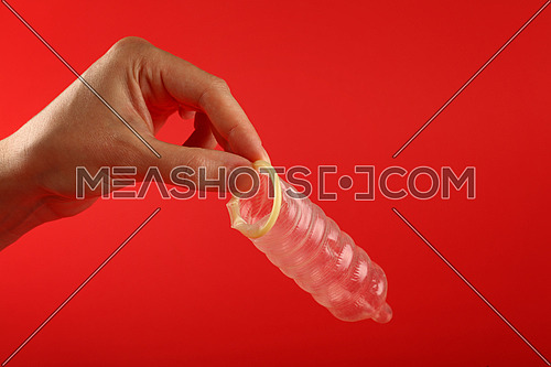 Close up man hand holding one open latex condom over red background with copy space, low angle side view