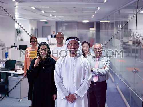 arabian famale and male business people standing as team in modern office with group of people in background