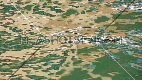 Close up abstract multicolor background of green and yellow reflections on water waves and ripples running at sea surface