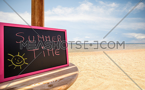 In the picture a beach umbrella which is small blackboard with the words ( Summer Time ) in a beach in the afternoon .