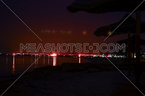 Long exposure view of the beach with lined hay sunshades and the city appears at the far end