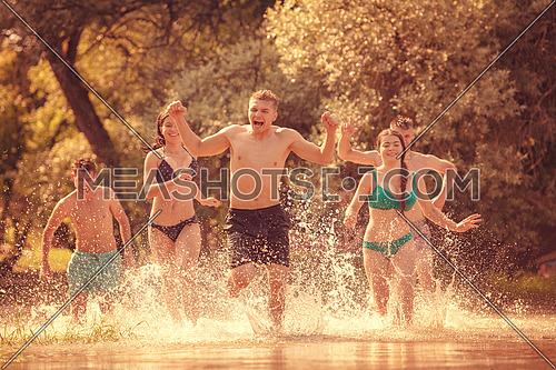 summer joy group of happy friends having  fun while running and splashing on river