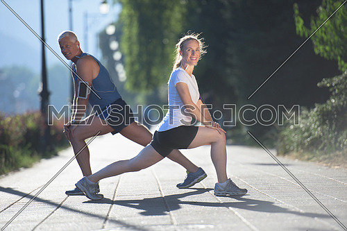 jogging couple warming up and stretching before morning running training workout  in the city with sunrise in background