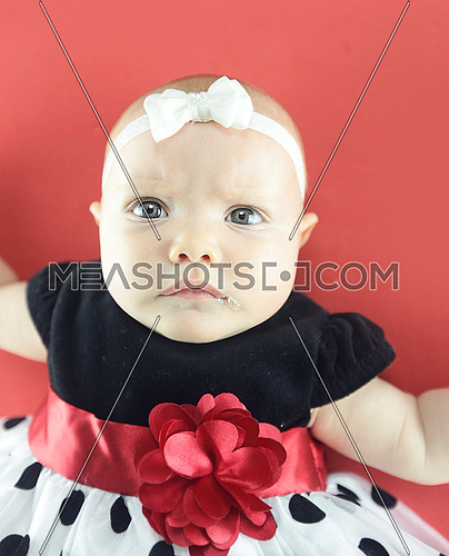 A cute baby wearing a dotted dress isolated on red