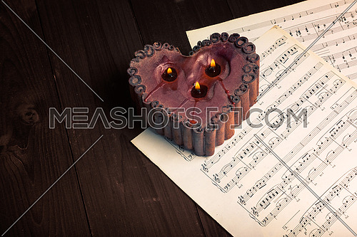 In the picture lit candle with the shape of heart, aged pages of sheet music and wooden background,used split tonig for old/vintage style.