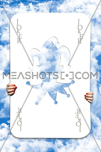 Large Joker Playing Card With Girls Hands Holding It In Sky Background