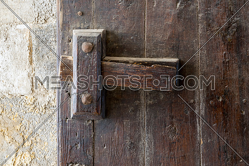 Front view closeup of a wooden aged latch over a wooden opened door