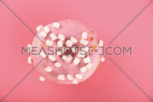 Round ring donut in pink glaze with small marshmallows topping decoration on pink paper surface