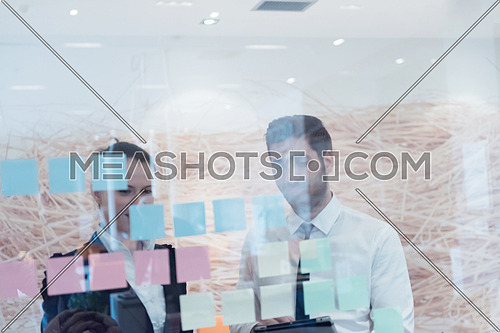young creative startup business people on meeting at modern office making plans and projects with post stickers on glass