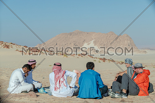 Group of tourists sitting with bedouin guides exploring Sinai Trail from Ain Hodouda at day.