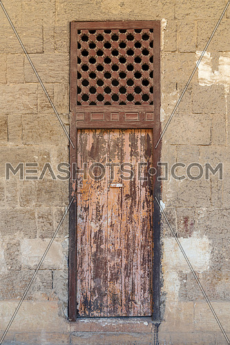 Facade of old abandoned stone bricks wall with weathered wooden door and windows covered with wooden grid, Old Cairo, Egypt