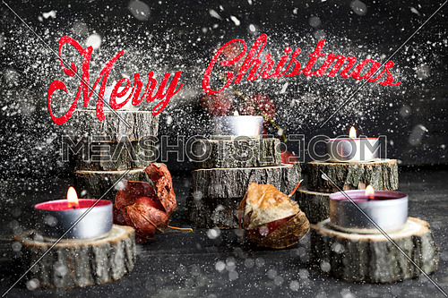 Merry Christmas. Christmas candles burning, decoration on wooden logs resting on rustic wooden background with Snow Flakes And Stardust