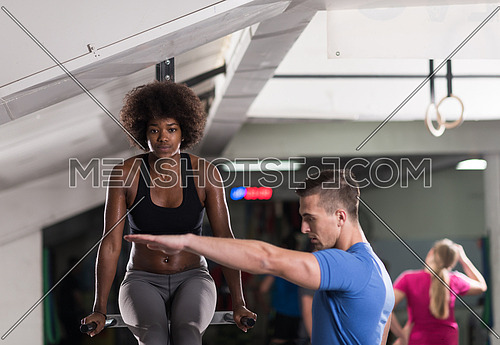 african american athlete woman workout out arms on dips horizontal parallel bars Exercise training triceps and biceps doing push ups with trainer