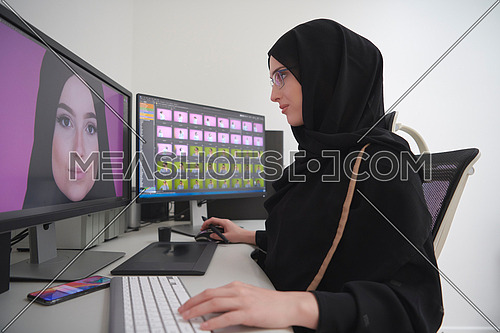 Young muslim girl working on the computer from home. Female photo editor at working place. Freelancer using two monitors while doing job