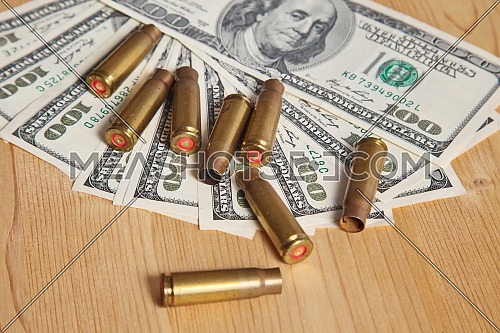 Closeup for used bullet shells and dollars on wooden table.