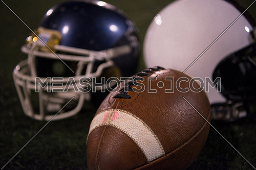 american football and helmets on grass field at night
