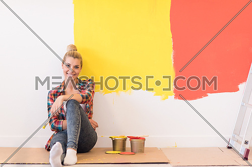 Portrait of a beautiful young female painter sitting on floor near wall after painting.