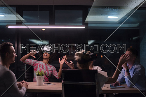 Multiethnic Business team using virtual reality headset in night office meeting  Developers meeting with virtual reality simulator around table in creative office.
