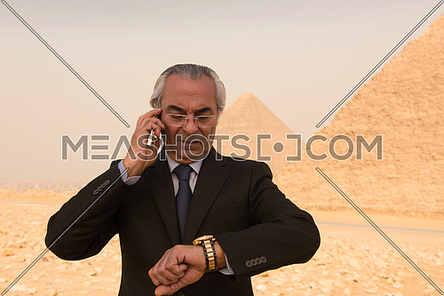 mature arab business man speeking over smartphone  with egyptian pyramids in background