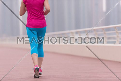 very active young beautiful woman busy running on the promenade along the ocean side with a big modern city in the background to keep up her fitness levels as much as possible