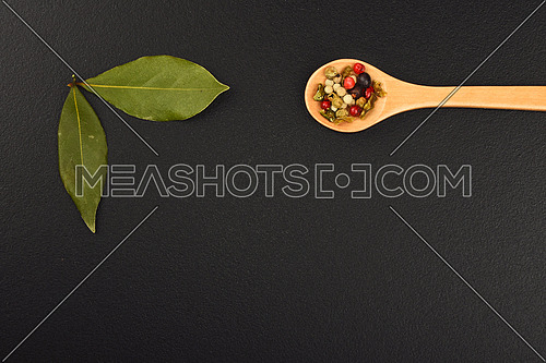 Group of bay two laurel leaves and mix of peppercorn in wooden spoon on black chalkboard background