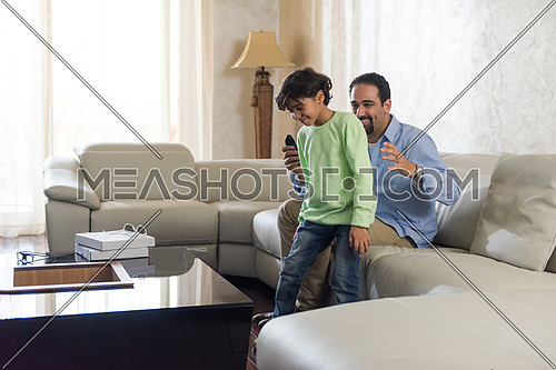 Middle Eastern father cheerfully spends time with his son on the sofa and enjoy watching tv