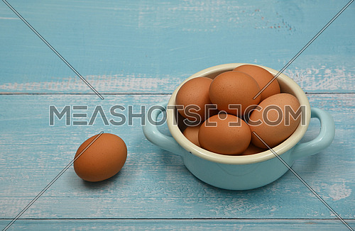 Close up metal pan bowl of brown chicken eggs on light blue rustic wooden table surface, high angle view