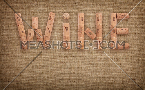 Word WINE shaped by natural wooden wine bottle corks of different vintage years over background of jute canvas